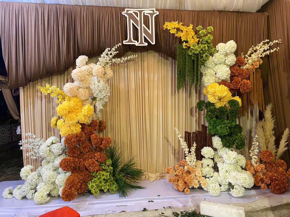 Backdrop hoa tông vàng cam có chữ lồng tên dâu rể